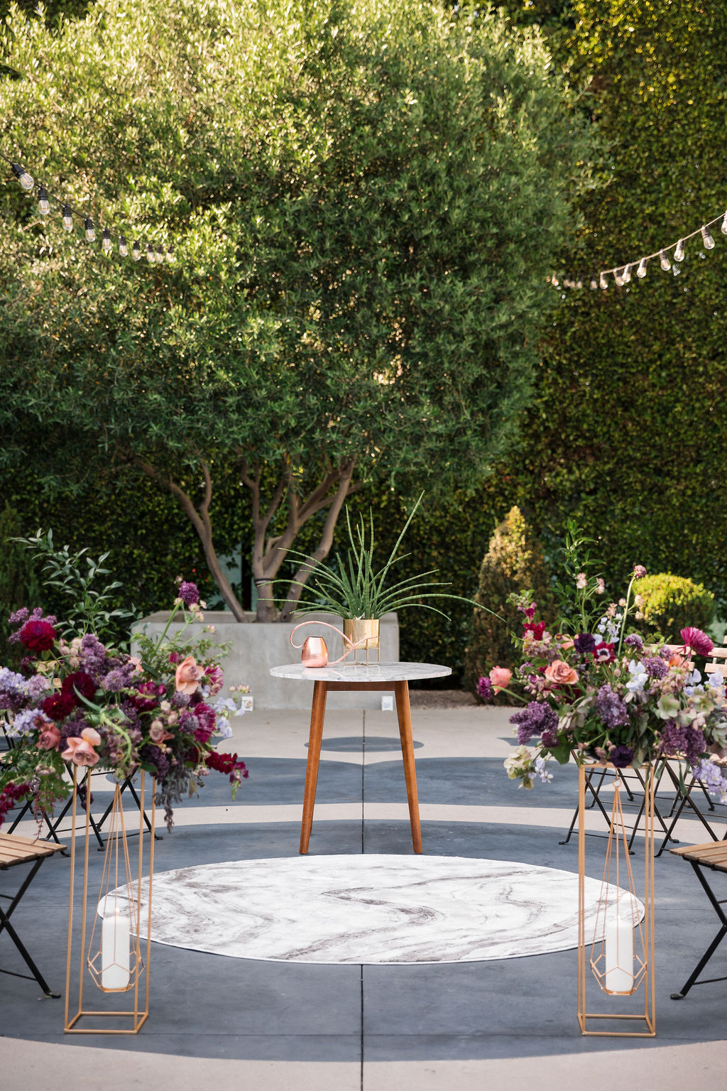 circle outdoor wedding ceremony seating at The Fig House courtyard with two gold geometric candle holders with pink and purple floral arrangements on tops
