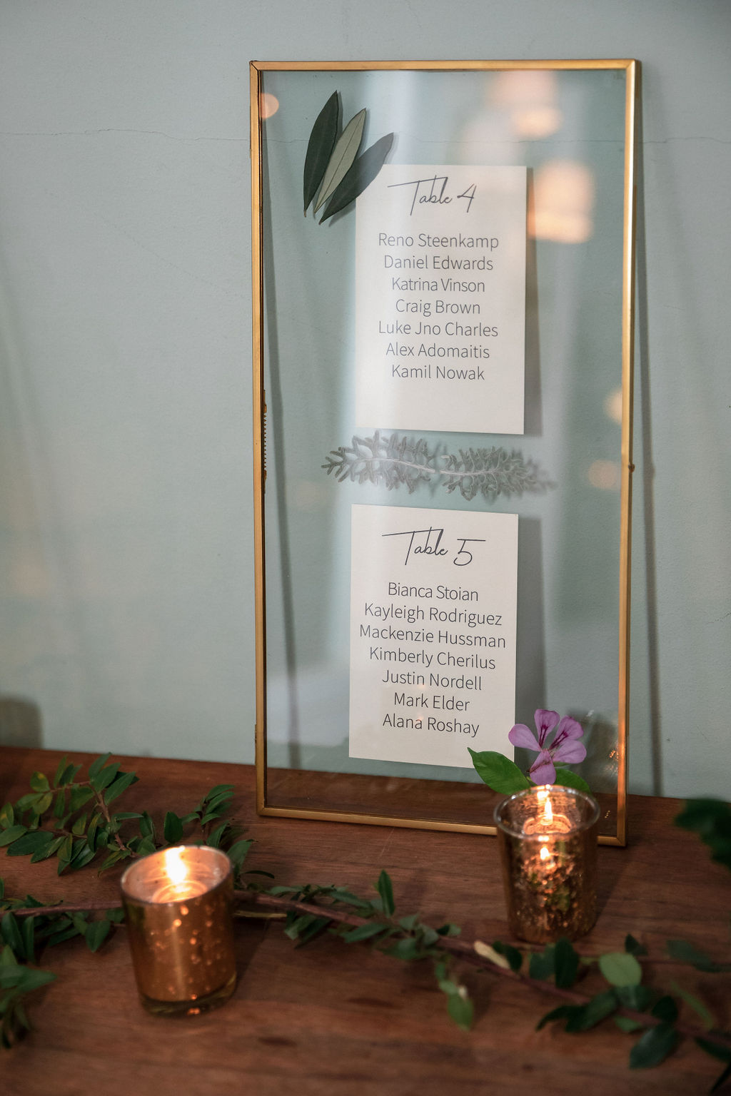 gold framed wedding seating chart with pressed flowers and greenery
