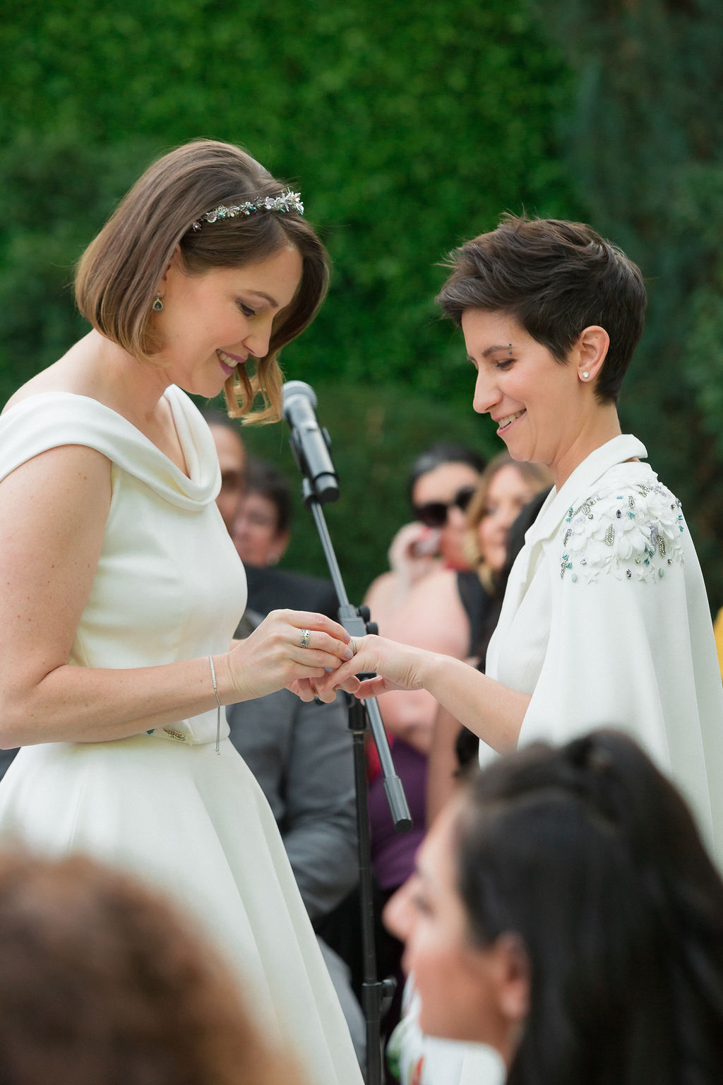two brides wearing coordinating bridal attire exchange rings during outdoor wedding ceremony at the Fig House