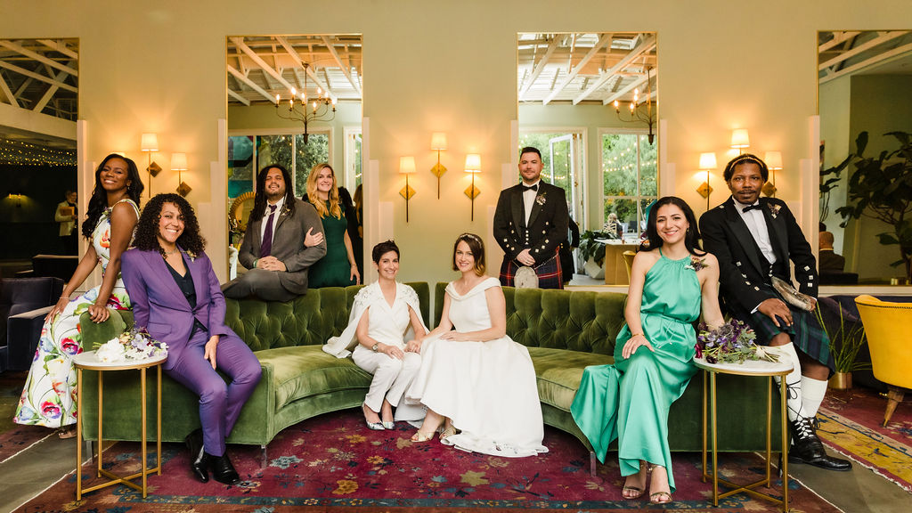 wedding party photo with brides in custom made bridal attire in the middle of a velvet green couch 