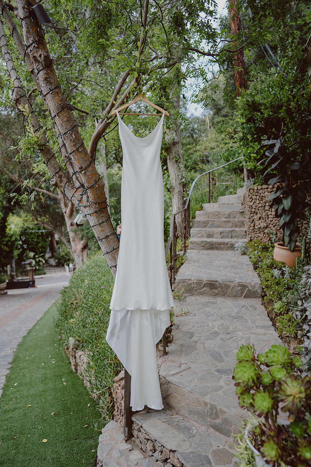 modern minimalist silk wedding dress hangs in trees next to stone staircase