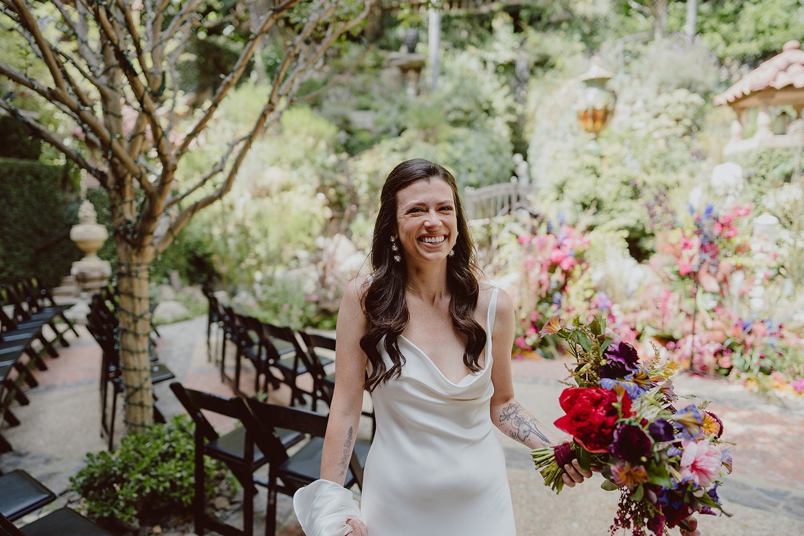 bride in minimalist satin wedding dress holds  bright colorful bridal bouquet