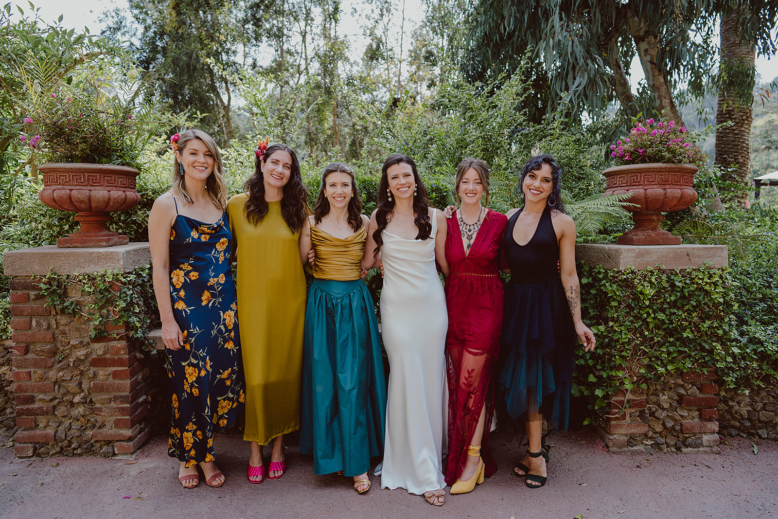 minimalist bride in silk wedding dress stands with bridesmaids in colorful mixed dresses