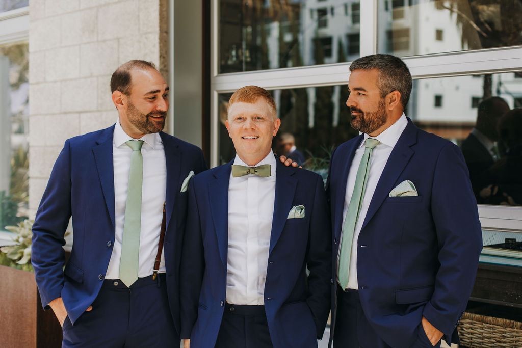 groom in navy blue suit with green bowtie stands with groomsmen in navy blue suits and green ties