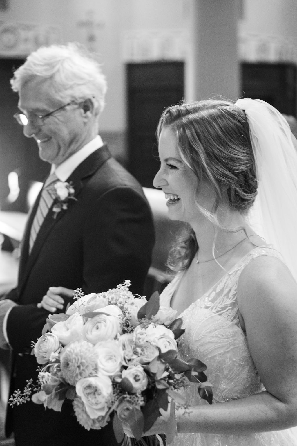 black and white photo of smiling bride walking down aisle with father of the bride