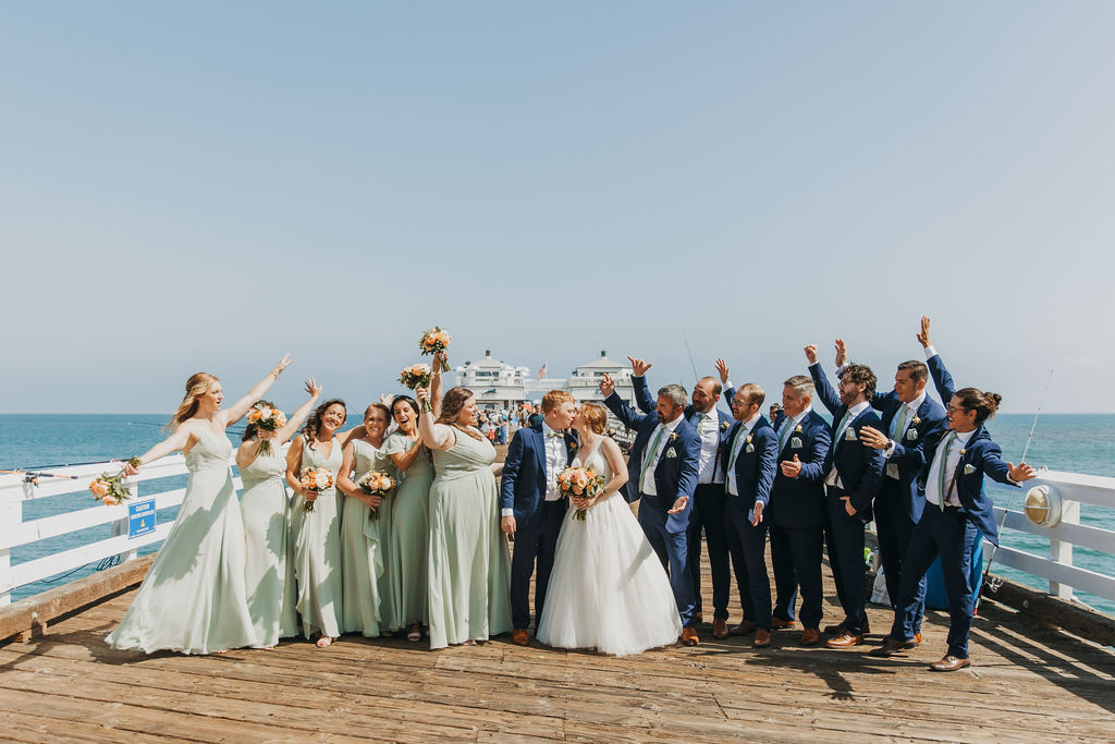 bride and groom with wedding party in mint green dresses and navy blue suits taking photos in Malibu pier