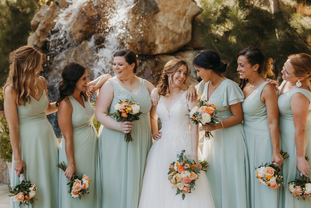 bride in v-neck tulle ball gown stands with bridesmaids in mint green dresses in front of waterfall at Calamigos Ranch