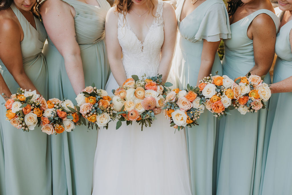 bride in v-neck tulle ball gown stands with bridesmaids in mint green dresses with bright orange bouquets in front of waterfall at Calamigos Ranch