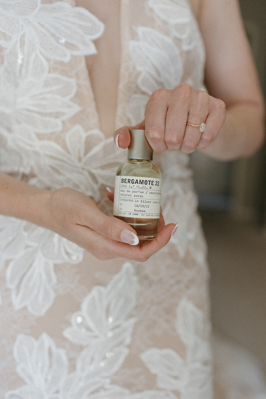 bride with oval cut diamond wedding ring holding a bottle of bergamot 22 perfume 