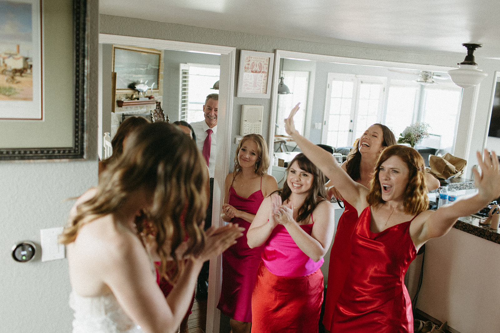 bride walks down staircase to do first look with bridesmaids in bright pink and red dresses 