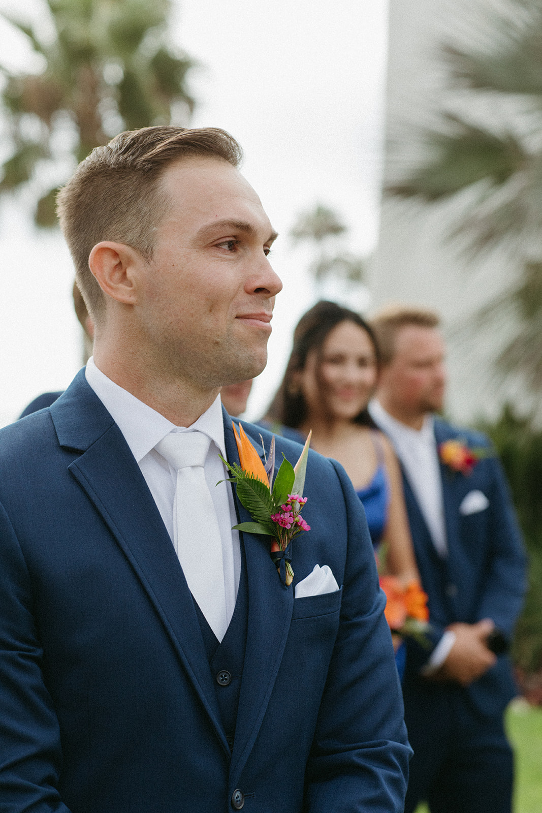 emotional groom in blue suit and white tie and tropical boutonniere watches bride walk down aisle 