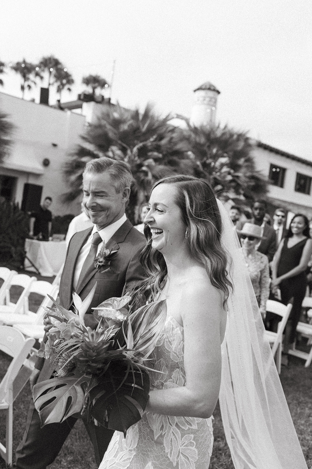 black and white photo of bride and father of the bride smiling as they walk down the aisle