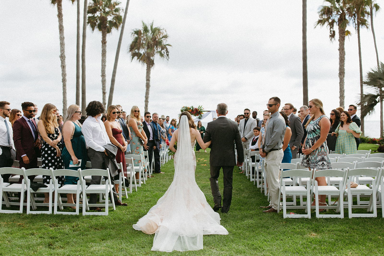 photo of brides train and chapel length veil walking down all grass wedding aisle during tropical wedding