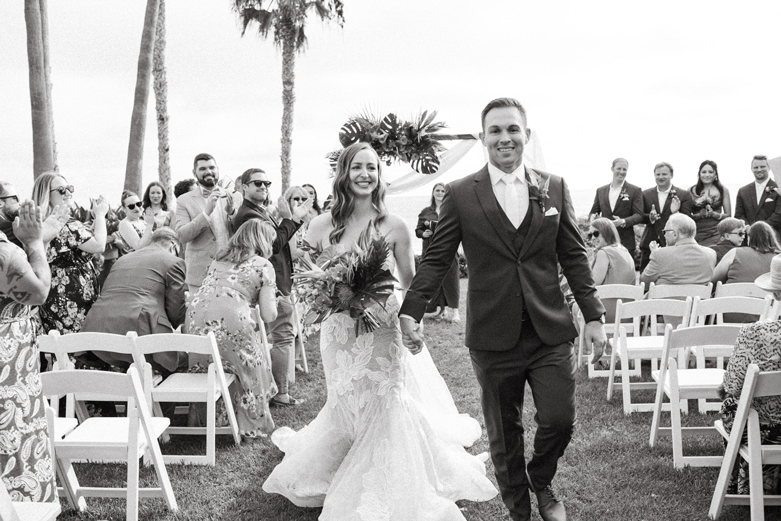 black and white photo of bride and groom during recession of tropical wedding ceremony at Ole Hanson Beach Club