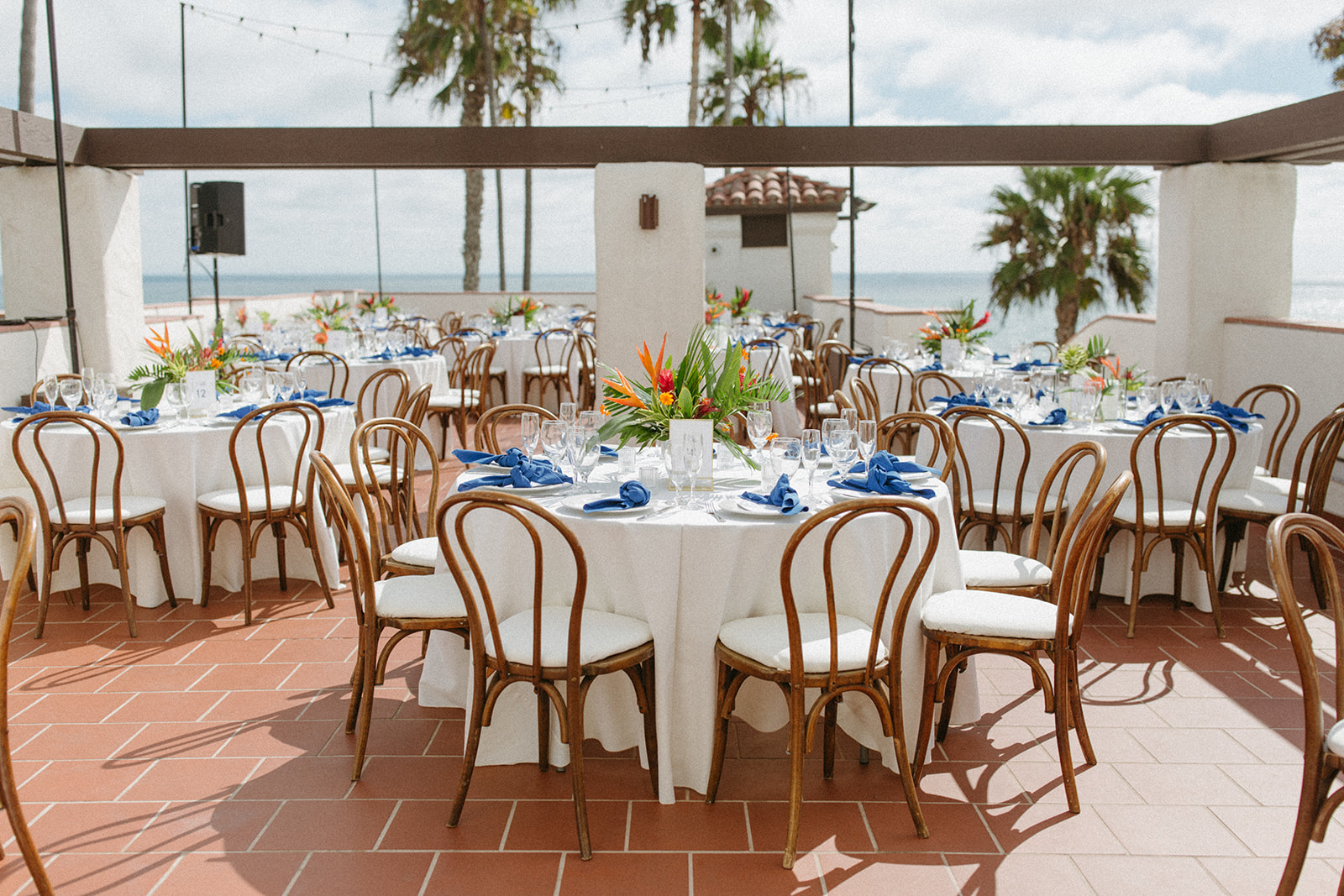 outdoor wedding reception at Ole Hanson Beach Club with wooden chairs and white linens, blue napkins and tropical floral table arrangements