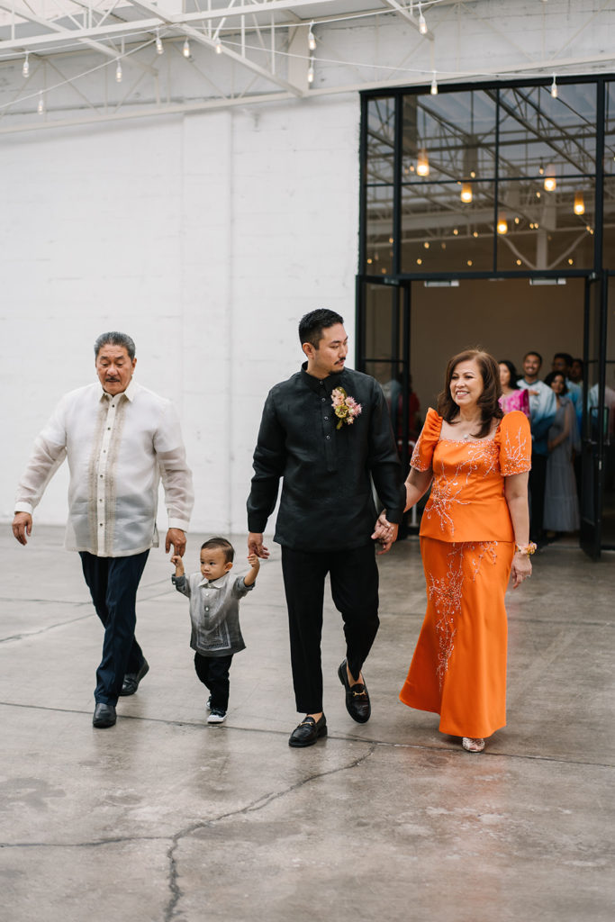 groom in all black suit walks with parents and toddler down ceremony aisle during cloud themed wedding