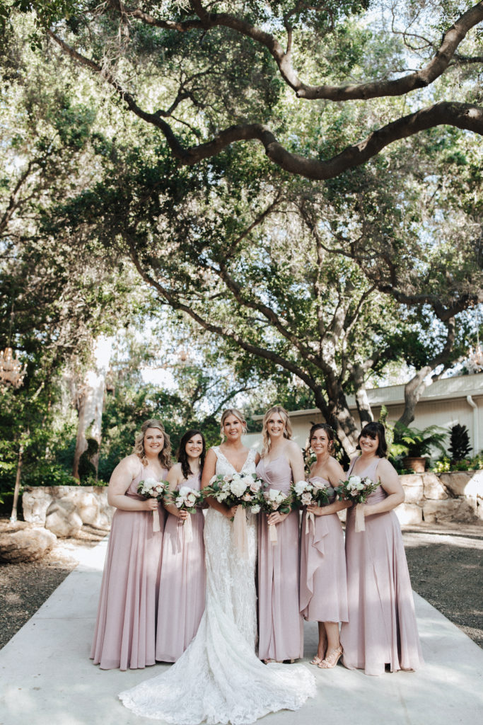 bride in champagne v-neck wedding dress with beaded lace overlay and soft pink and white bridal bouquet stands with bridesmaids in mixed pink dresses for spring wedding at Calamigos Ranch