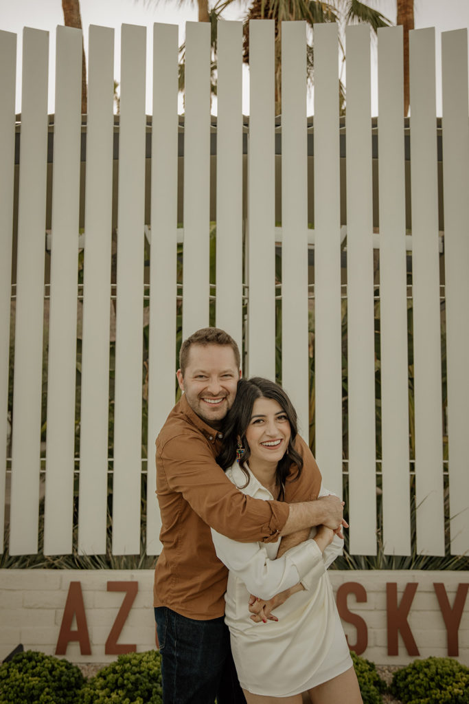 mid-century inspired desert engagement photo session with bride to be in silk mini dress and groom in brown button up in front of white fence