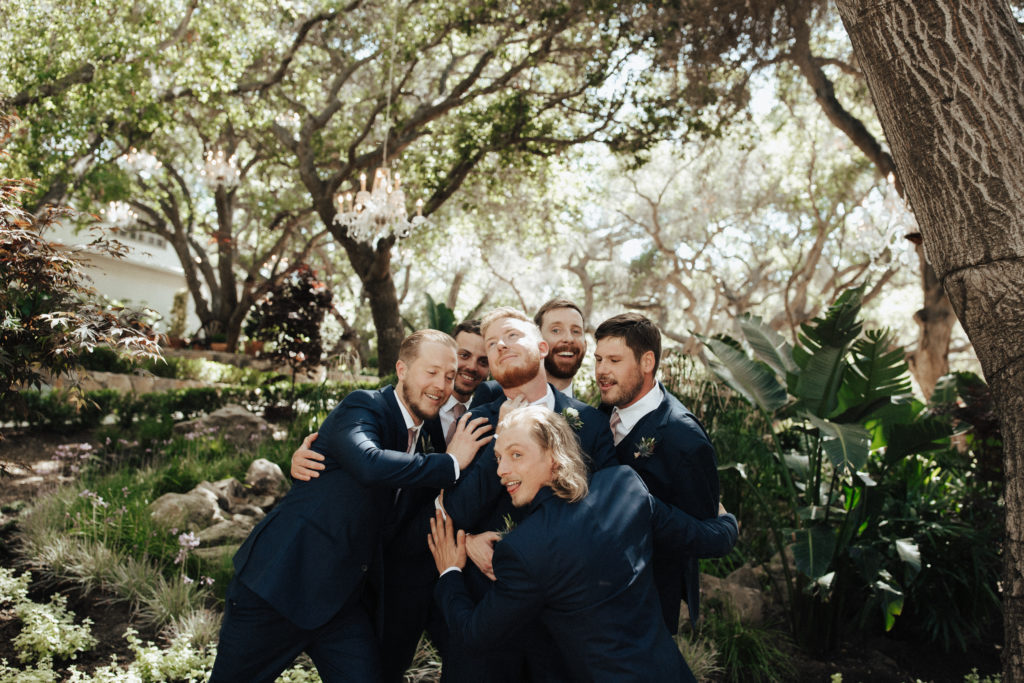 groom and groomsmen in black suits with soft pink bow ties stand in garden at Calamigos Ranch