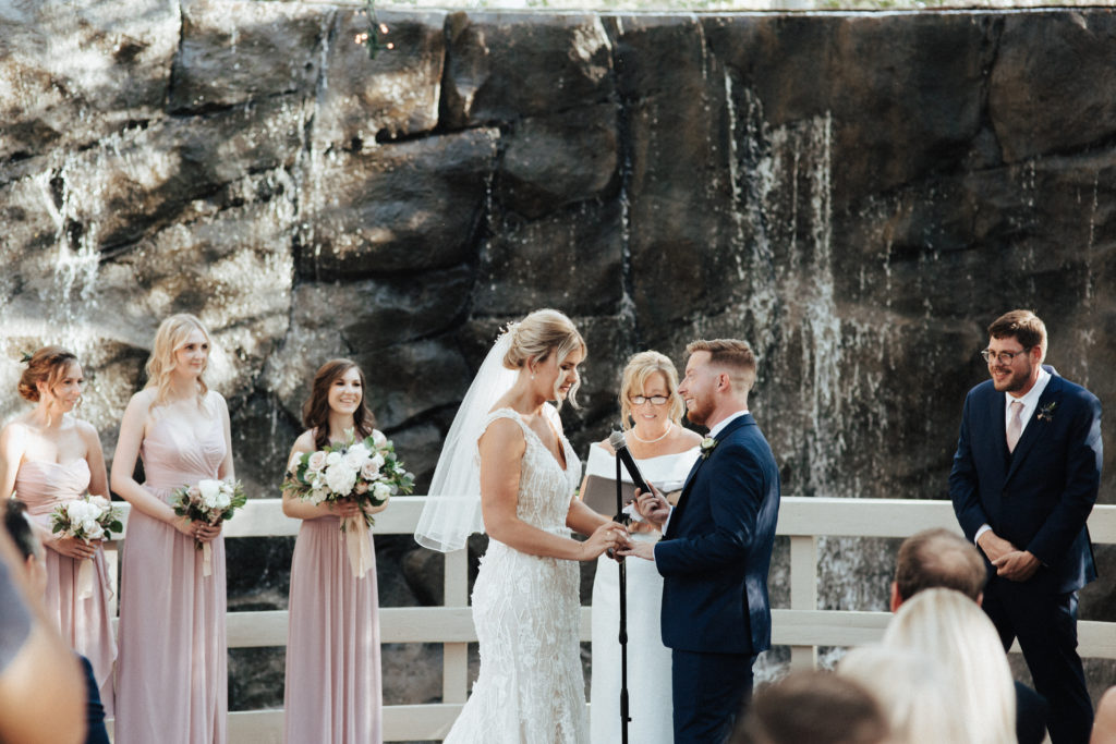 spring wedding ceremony in front of waterfall with soft pink and white flowers at Calamigos Ranch Oak Room