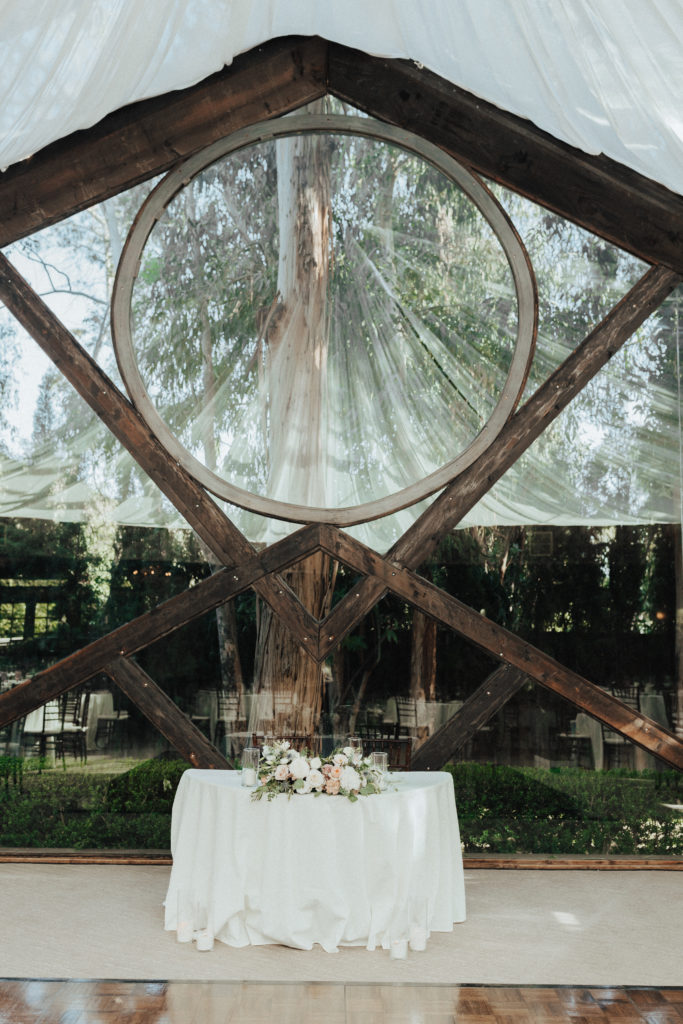 sweetheart table with white linen and soft pink and white floral arrangement in front of Oak Room cathedral window 