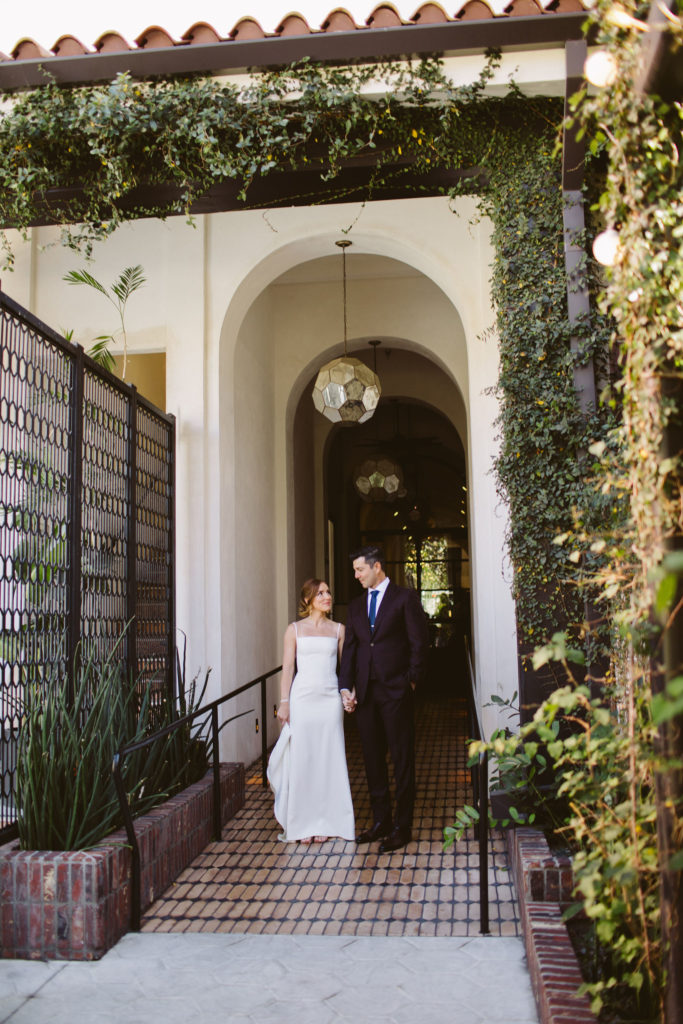 bride in modern square neck spaghetti strap wedding dress and groom in deep plum suit take portrait shots at Hotel Figueroa