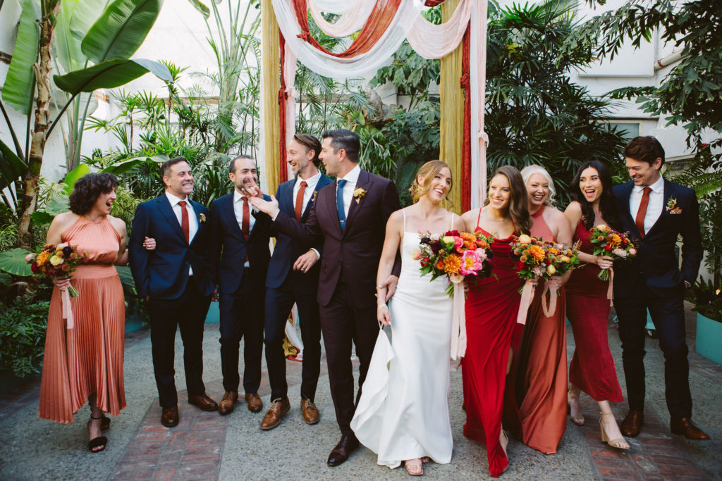 bride and groom stand with co-ed wedding party in front of earth toned ceremony drapery 