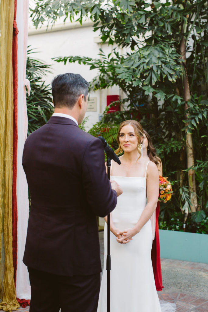 groom in plus suit with blue tie reads vows to bride in modern square neck wedding dress with spaghetti straps and cathedral veil during wedding ceremony at Valentine DTLA