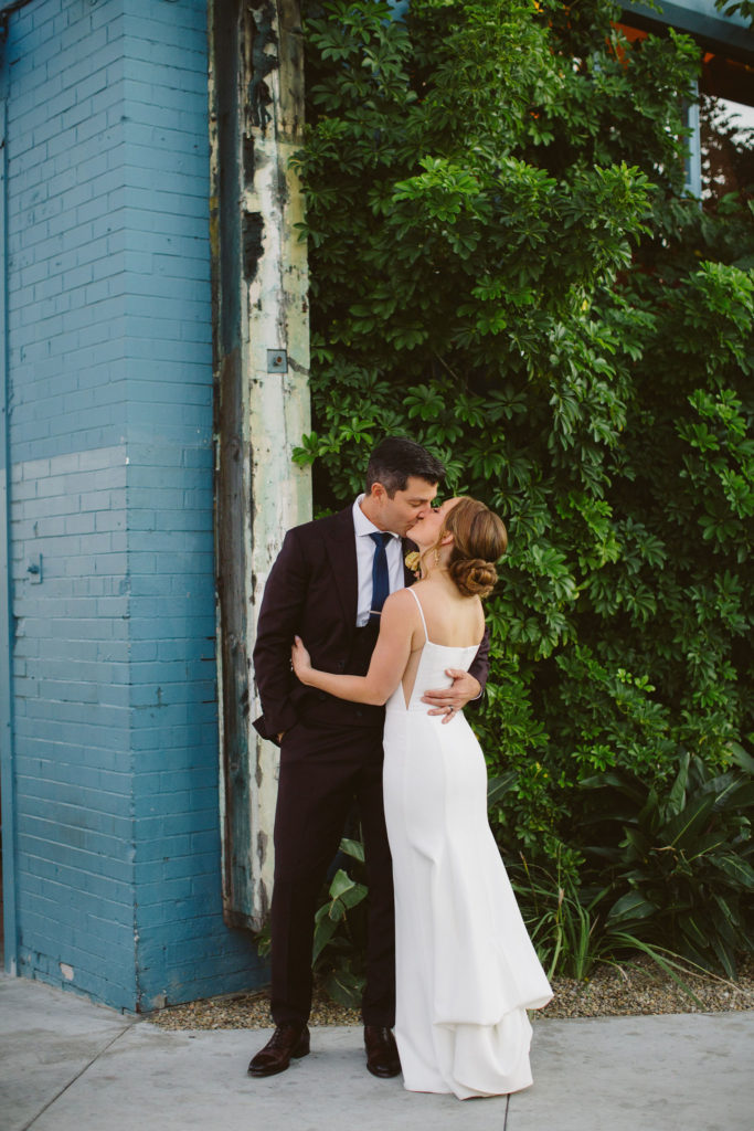 bride in modern square neck wedding dress with spaghetti straps takes photos with groom in plum suit and blue tie