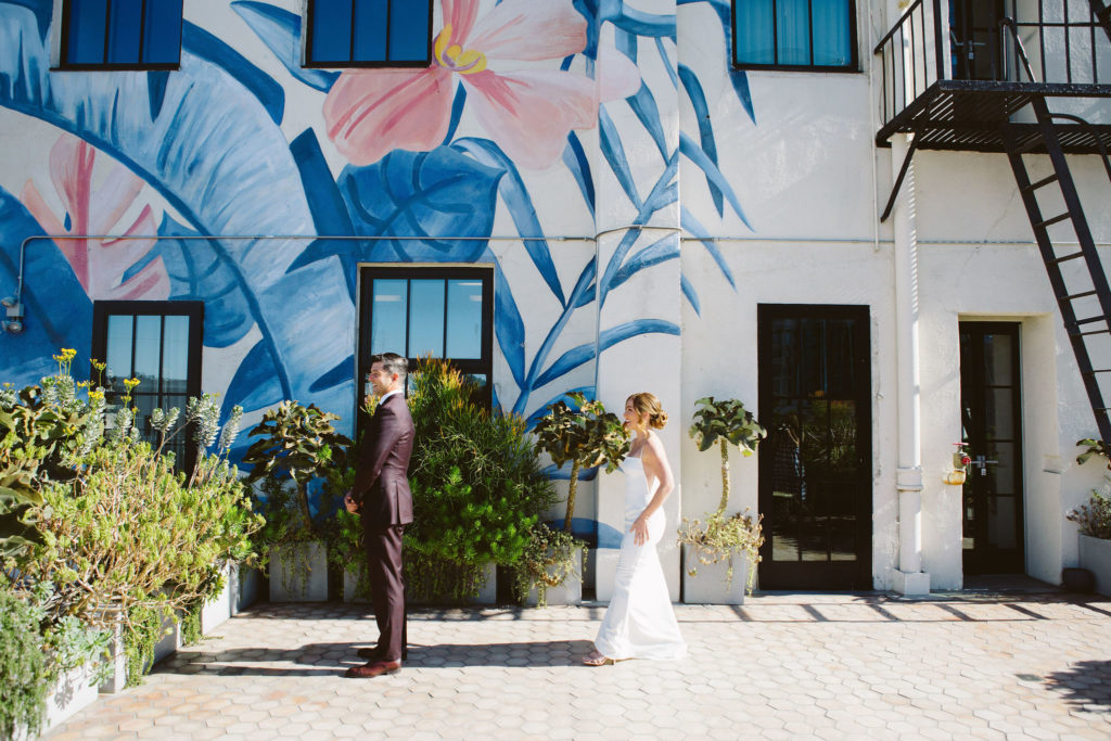bride in modern square neck spaghetti strap wedding dress and groom in deep plum suit have first look outside at Hotel Figueroa