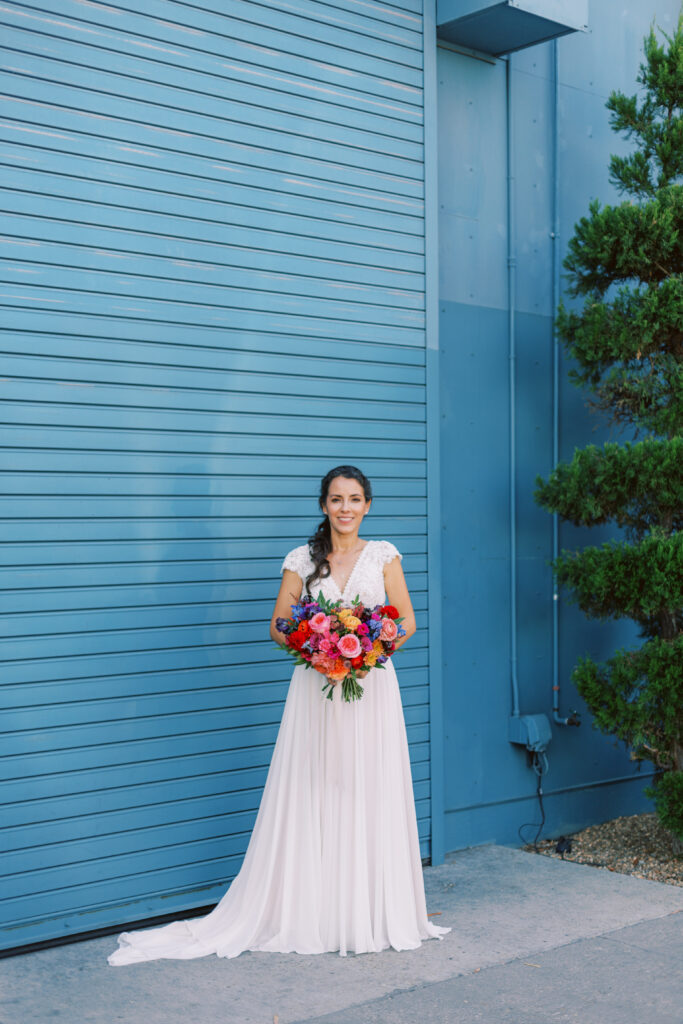 bride in lace bodice wedding dress with short sleeves holding brightly colored bridal bouquet