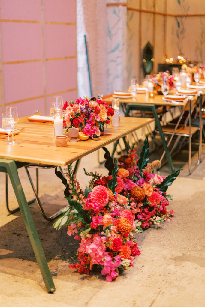 fiesta themed wedding reception with brightly colored floral arrangements, orange linens and table numbers with Spanish tile inspired artwork