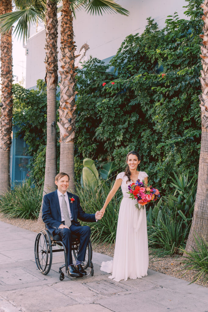 bride in short sleeve v-neck lace bodice wedding dress with groom in blue suit and colorful boutonniere taking portrait shots outside of Grass Room DTLA