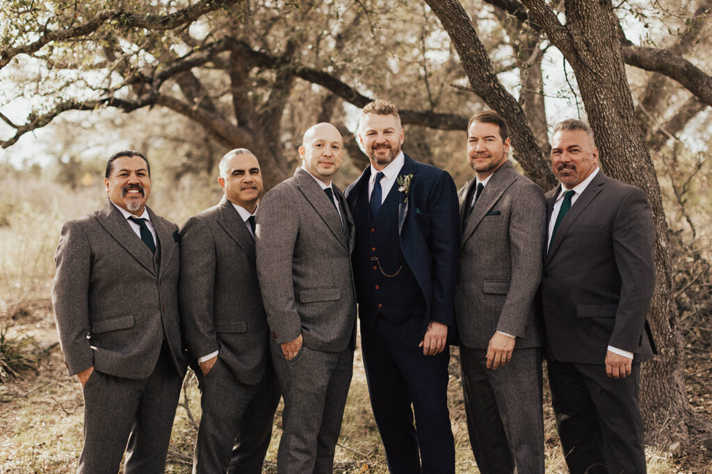 groom in navy blue suit stands with wedding party in charcoal grey suits 