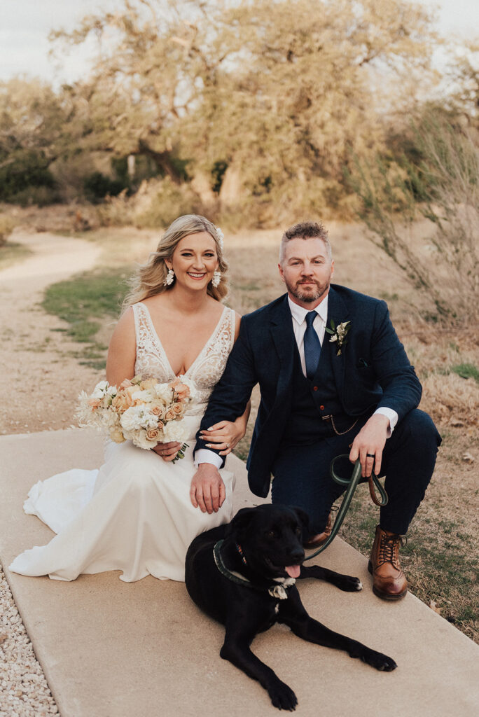 bride in deep v neck wedding dress with lace cut out and groom in navy blue suit pose with their dog