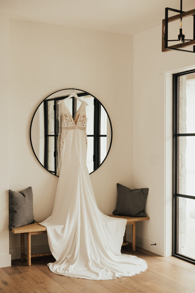 deep v neck wedding dress with lace and train hanging by mirror