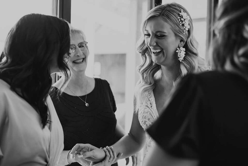 black and white photo of bride with soft beach waves and crystal hair piece laughing with mother and wedding party