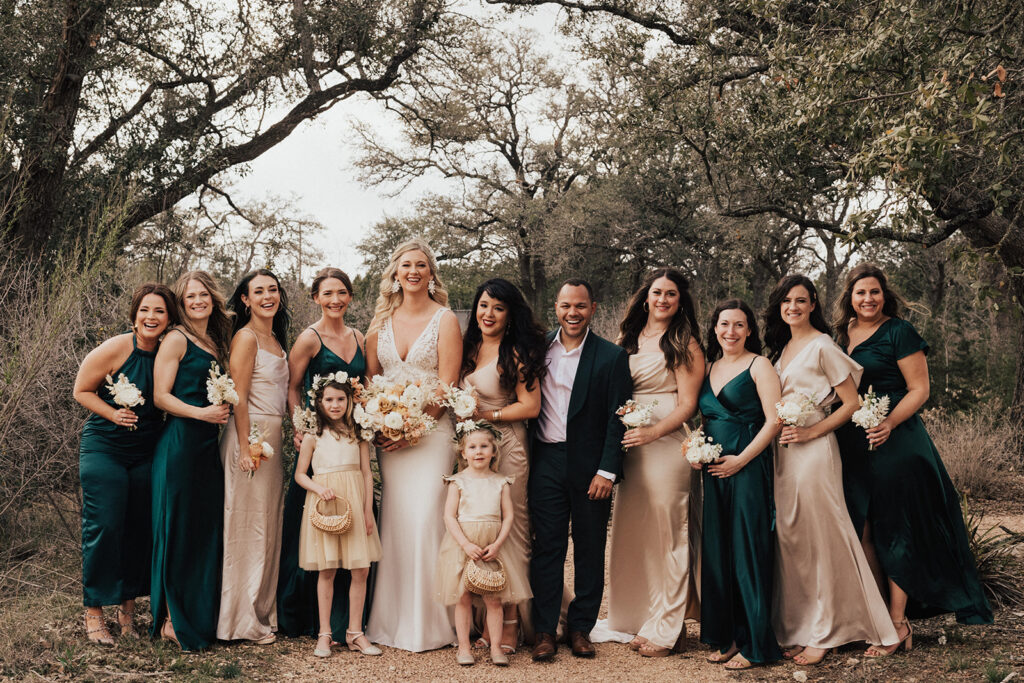 bride in deep v neck wedding dress with lace cut outs stands with wedding party in mixed Champagne and green attire