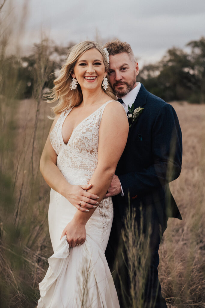 bride in deep v neck lace wedding dress with groom in navy blue suit