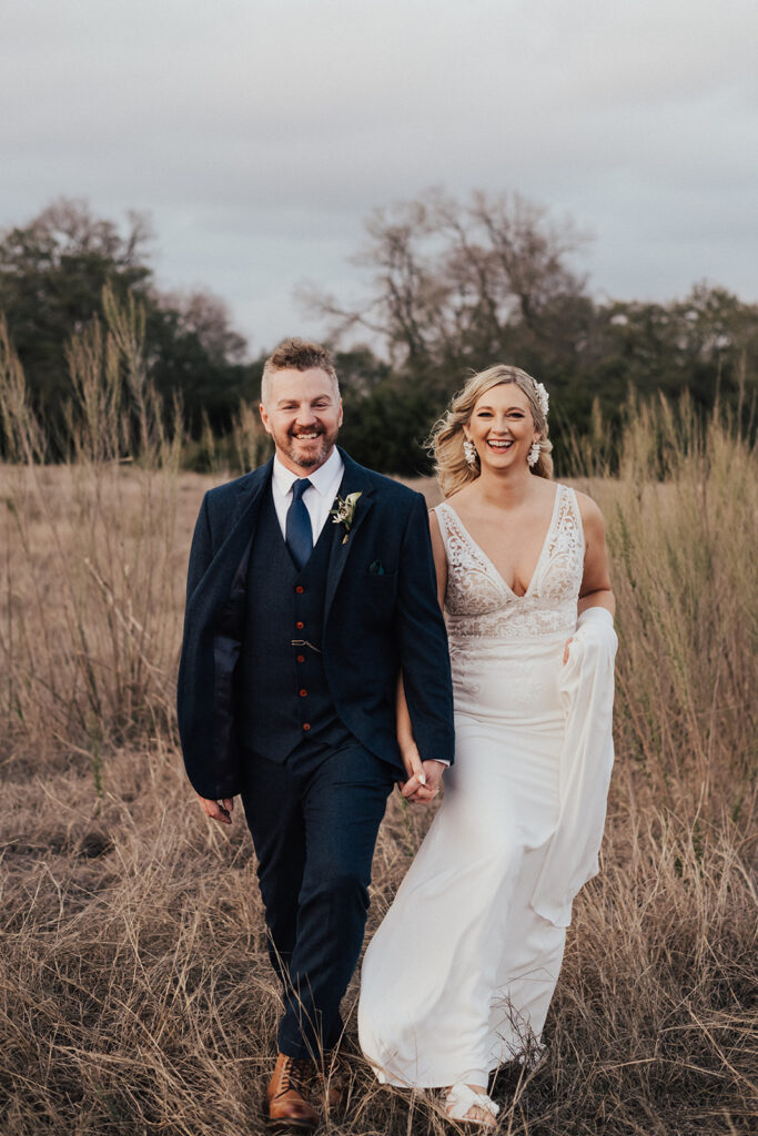 bride in deep v neck lace wedding dress holds hand with groom in navy blue suit