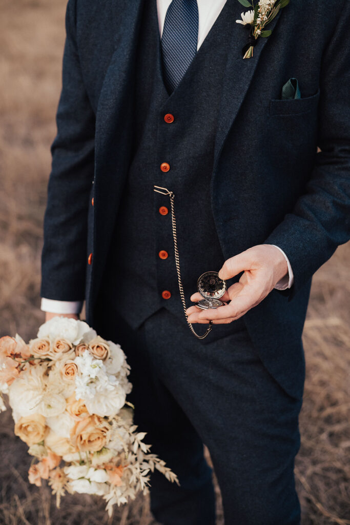 groom in navy blue suit holds pocket watch