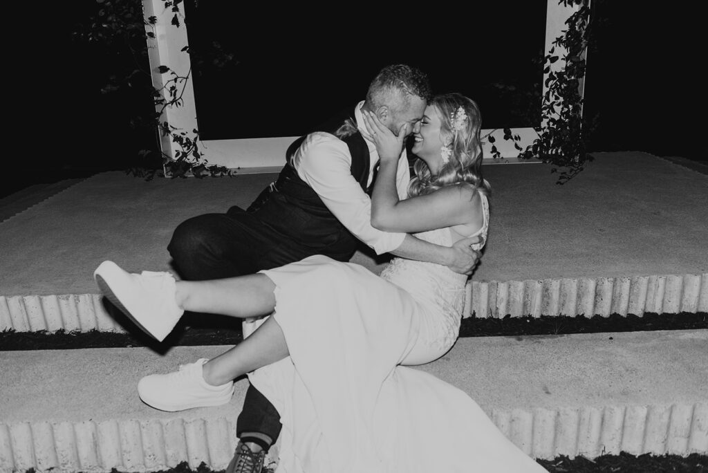 black and white photo of bride in sneakers kissing groom on ceremony steps during wedding reception